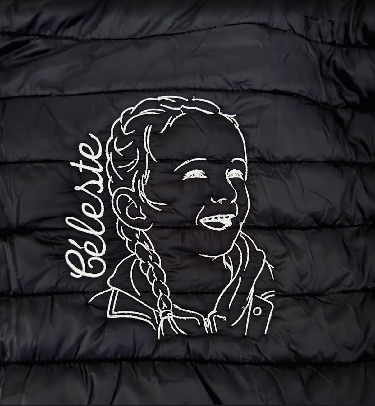 Portrait et prénom brodés en fil blanc sur une doudoune noire
