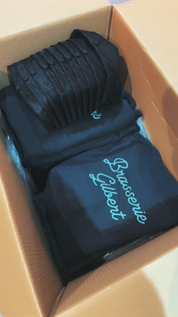 Tee-shirts bleu marine avec un logo turquoise, rangés dans un carton